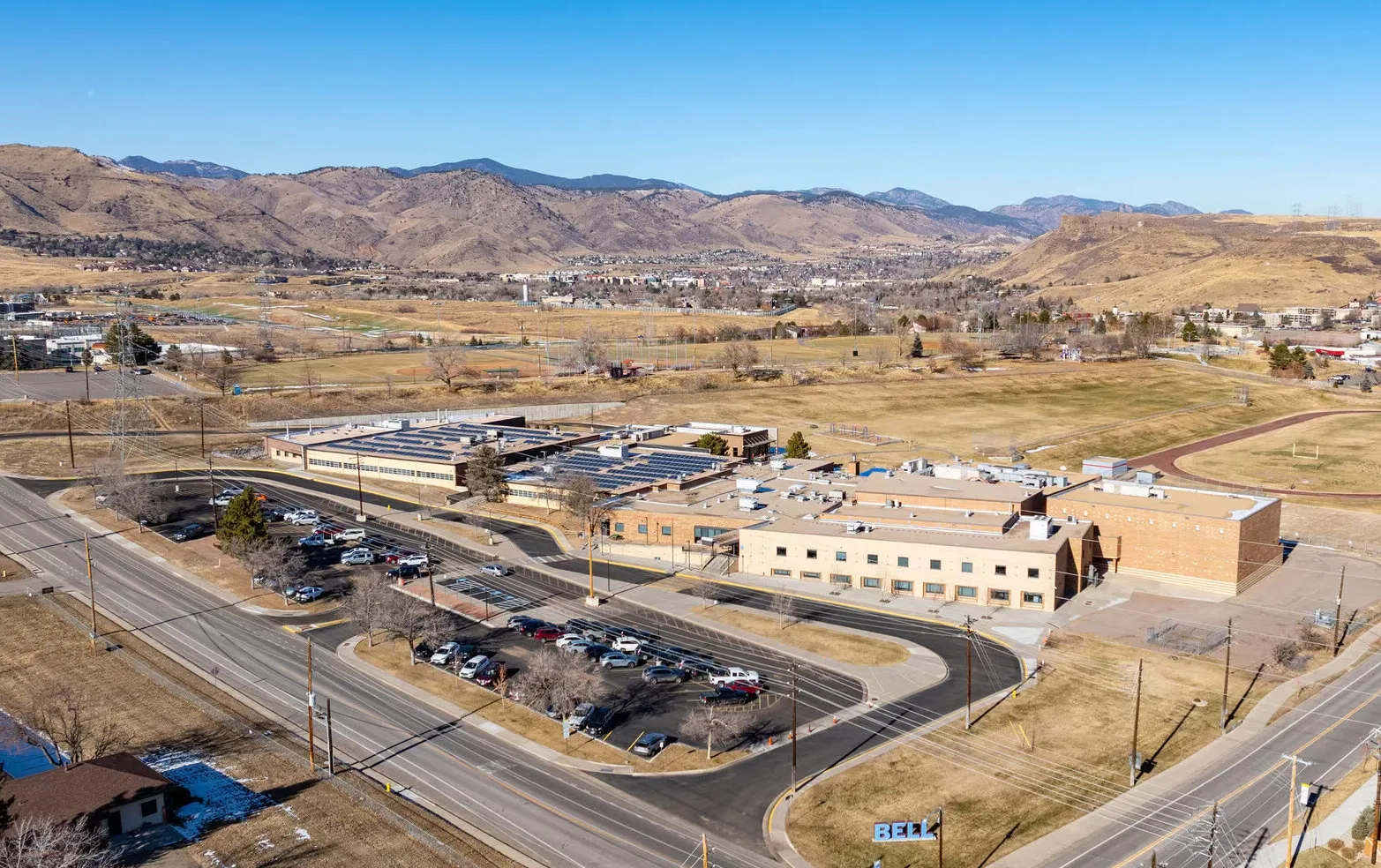 Bell Middle School exterior with students arriving beneath the red-brick facade and mountain backdrop.