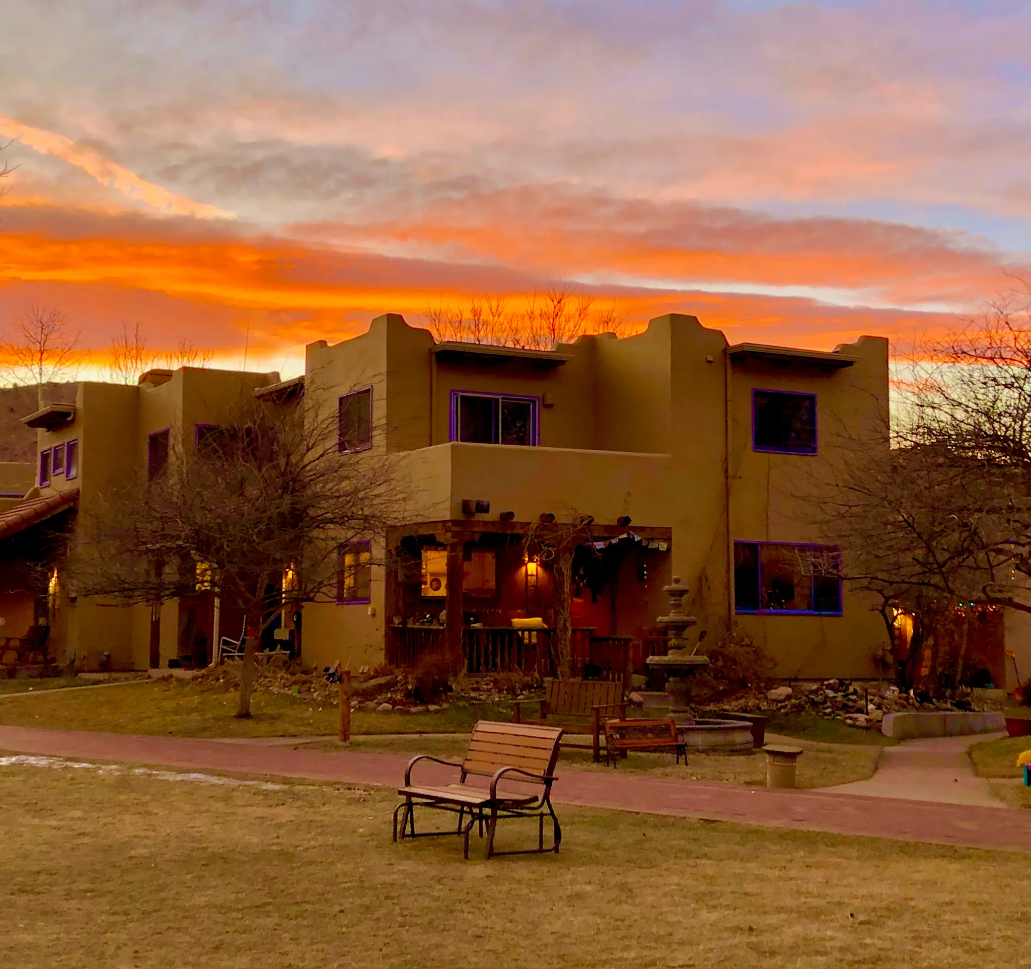 The Common House at sunset with dramatic golden and orange sky, benches in foreground for quiet reflection