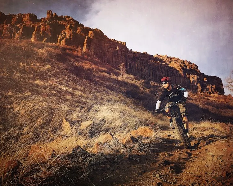 Mountain biker descending the basalt cliffs of North Table Mountain at sunset.